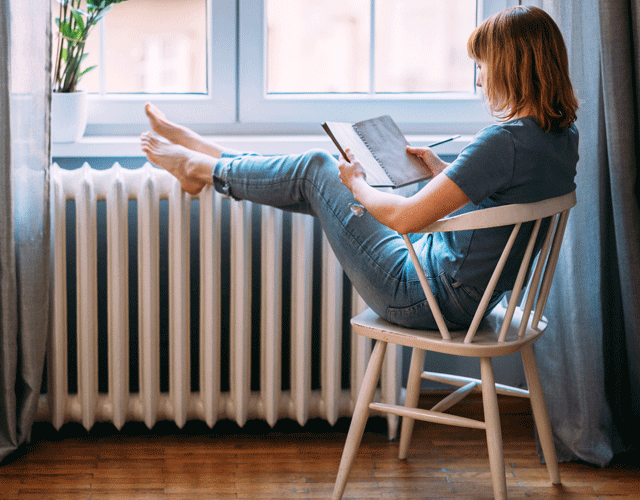 Frau sitzt vor einer Heizung