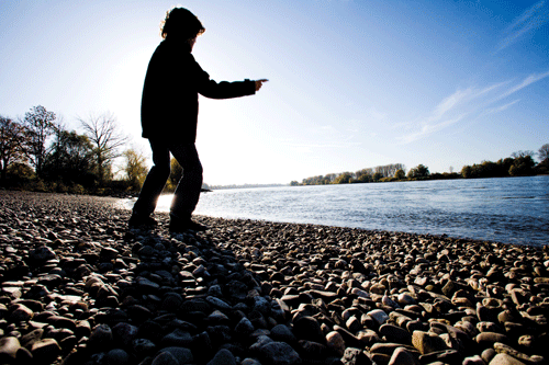 Mann steht auf Kieselstrand am Rhein